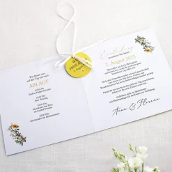 Einladungskarte zur Hochzeit mit Blütenkranz und rundem Anhänger